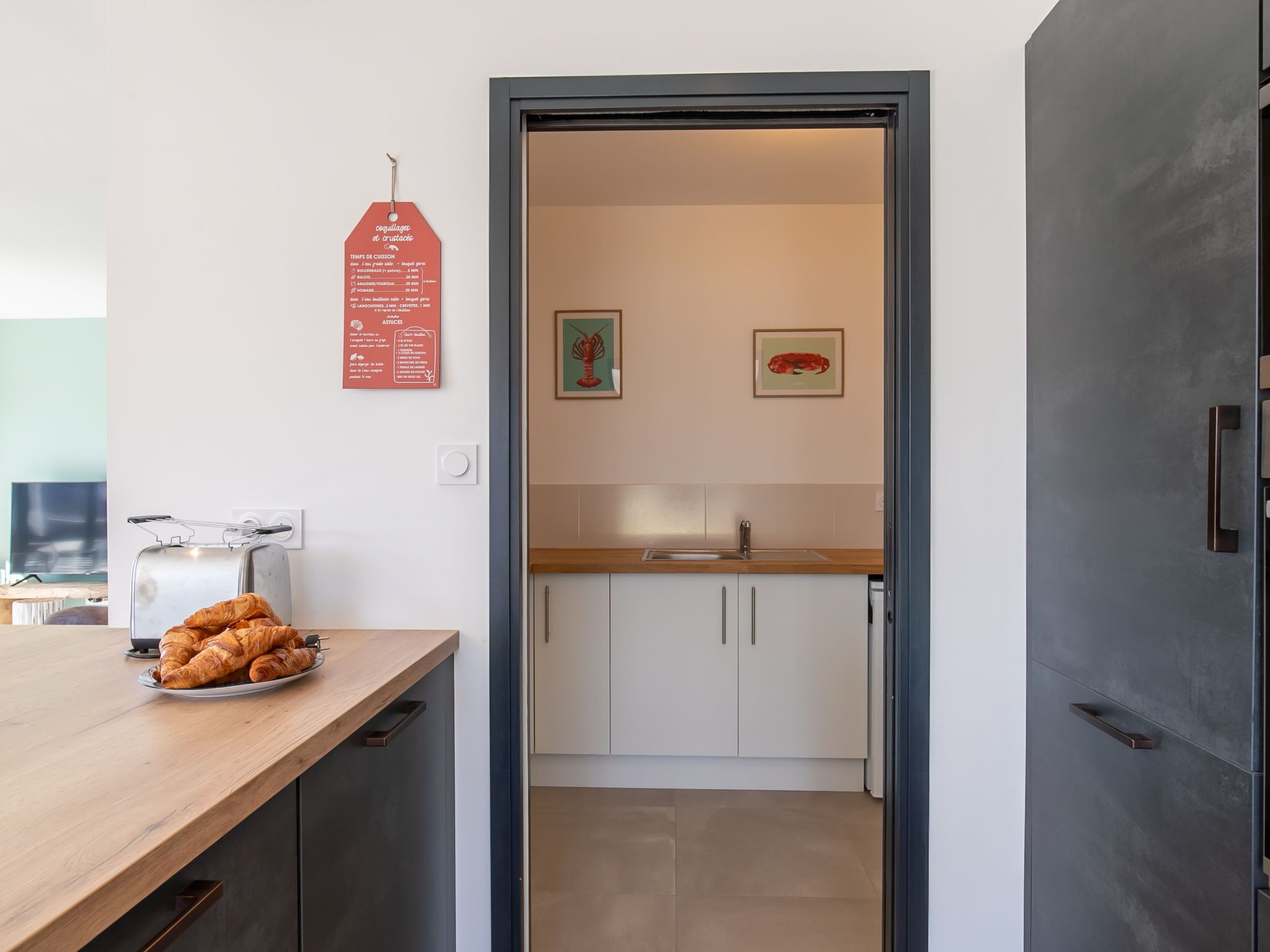 A modern kitchen with white cabinets, a wooden countertop, and a toaster. There is a plate of croissants on the counter.
