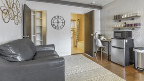 Un salon moderne avec un canapé en cuir, une horloge et un coin cuisine équipé d’un réfrigérateur et d’un four à micro-ondes.