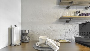 Une cuisine équipée d’une machine à café, d’une pile d’assiettes blanches, d’une serviette en tissu et d’une étagère où sont rangées des tasses et des bols.
