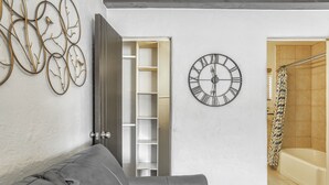 Un salon avec un canapé en cuir gris, une horloge murale, une décoration murale en métal et un dressing.