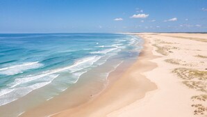 A wide sandy beach with gentle waves, a clear sky, and distant dunes. - Ocean on the Rocks, 1,21 Ocean Ave - waterfront, Wi-Fi, Ducted Air Conditioning (Anna Bay)