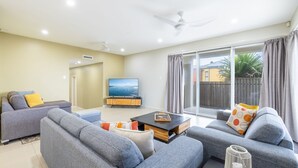 A modern living room with grey sofas, a flat-screen TV, and a sliding glass door leading to a balcony. - Ocean on the Rocks, 1,21 Ocean Ave - waterfront, Wi-Fi, Ducted Air Conditioning (Anna Bay)