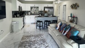 A modern kitchen with white cabinets, a central island with bar stools, a ceiling fan, and a marble floor.