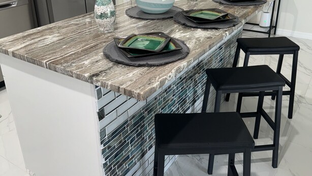 A kitchen island with a marble countertop, black bar stools, and a decorative vase.