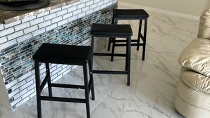 A kitchen with a marble countertop, two black stools, and a decorative vase with dried plants.