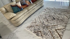 A beige leather sofa with colorful throw pillows and a patterned rug on a marble floor.