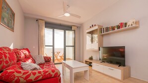 A living room with a red sofa, a white coffee table, a flat-screen TV, a ceiling fan, and a bookshelf with books and decorative items. - PARAISO COSTERO  - Cosy flat with shared pool (Conil de la Frontera)