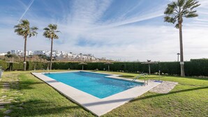 A rectangular swimming pool with a clear blue water, surrounded by a well-maintained lawn and palm trees. - PARAISO COSTERO  - Cosy flat with shared pool (Conil de la Frontera)