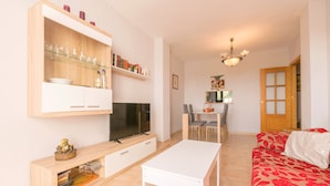 A living room with a TV, a white table, a red sofa, and a dining area with chairs and a table. - PARAISO COSTERO  - Cosy flat with shared pool (Conil de la Frontera)