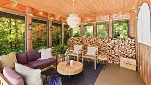 Ein gemütliches Interieur mit Holzbalkendecke, einer Couch, Sesseln, einem runden Tisch und einem Holzstoß.