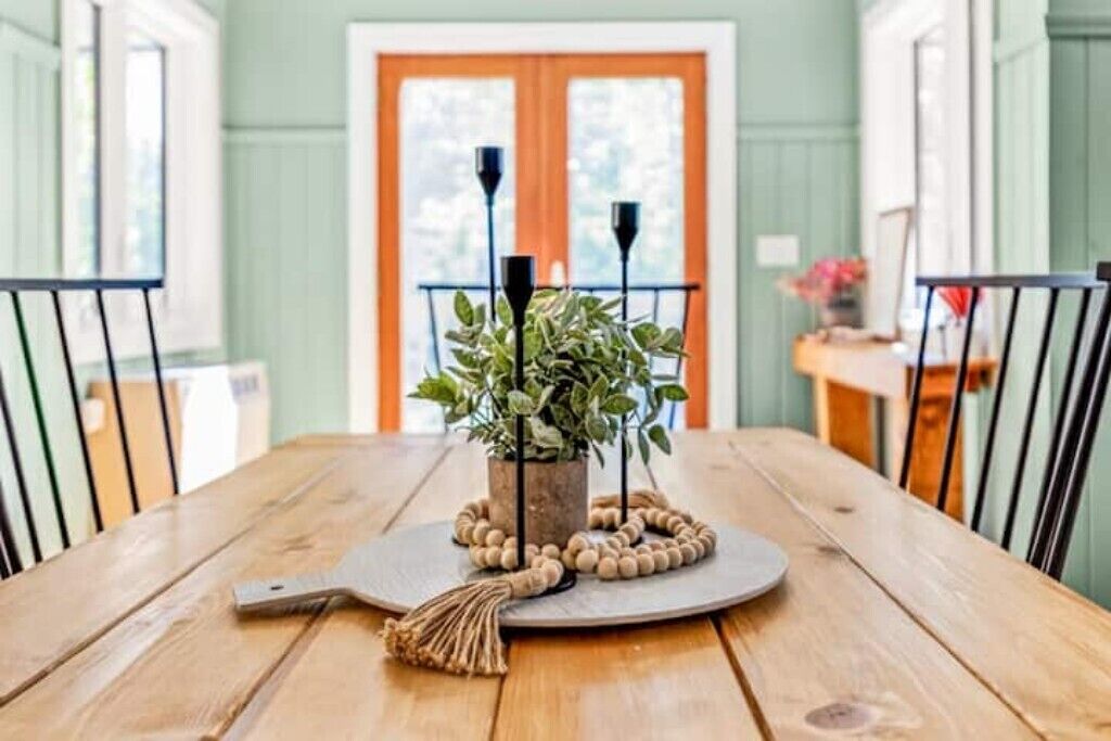 A wooden dining table with a central plant and candle holders, surrounded by chairs.