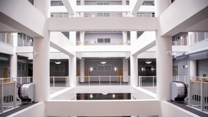 Ein mehrgeschossiges Atrium mit einem zentralen, offenen Bereich, Geländern und Rolltreppen.