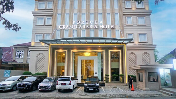 Das Hotel Portola Grand Arabia mit einer imposanten Eingangshalle, mehreren parkenden Autos und einem draußen stehenden Sicherheitsdienst.