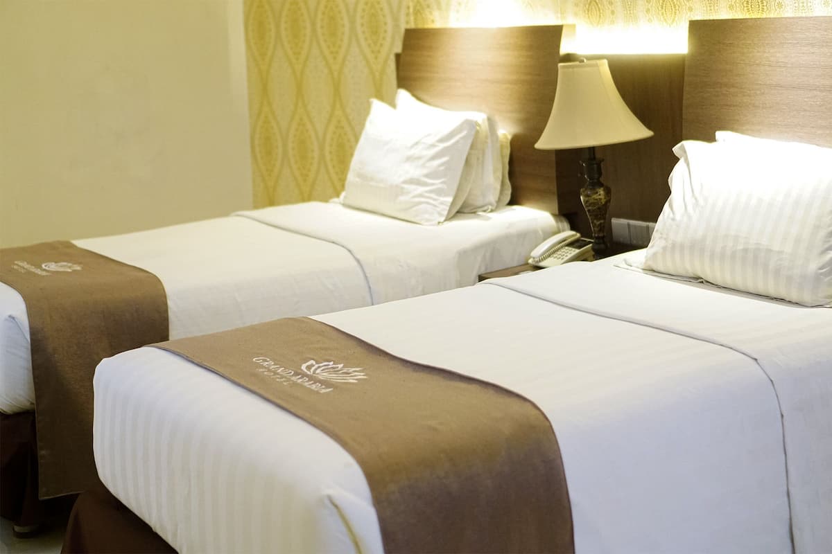 Dos camas de hotel con sábanas blancas y cabeceras marrones, una lámpara de noche y un teléfono sobre la cama de la izquierda.