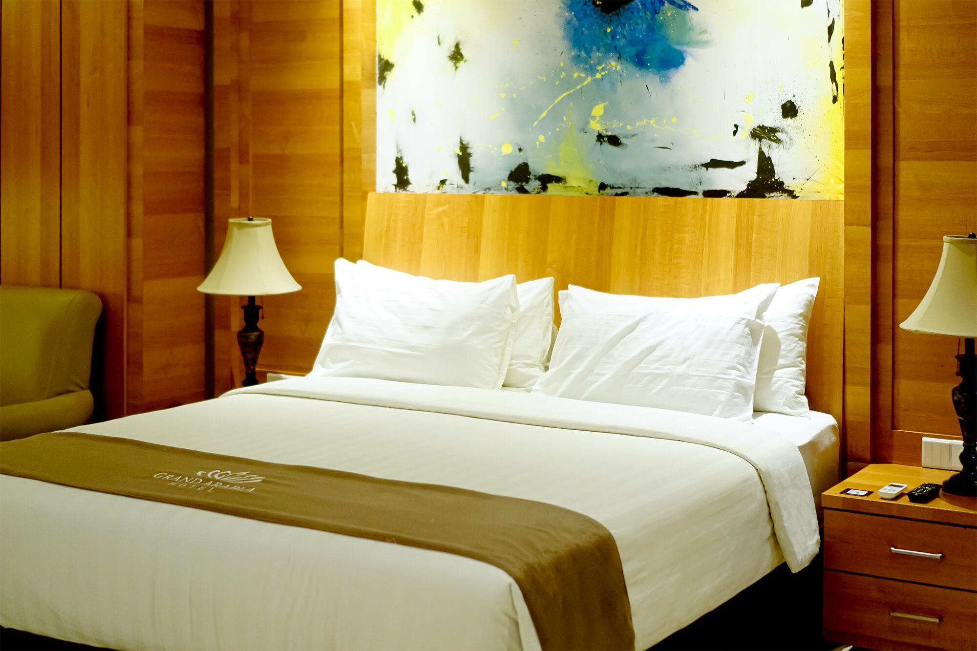 A hotel room with a bed, two bedside lamps, a nightstand, and a painting on the wall.