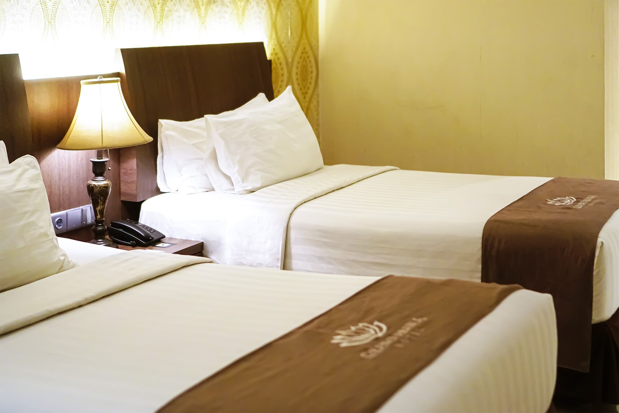 A hotel room with two beds, a bedside table with a lamp, and a telephone.