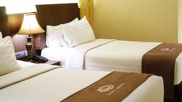 A hotel room with two beds, a bedside table with a lamp, and a telephone.