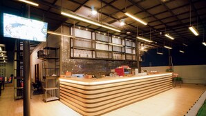 Eine moderne Bar mit Holztresen, Deckenbeleuchtung und einem großen Bildschirm, der Inhalte anzeigt.