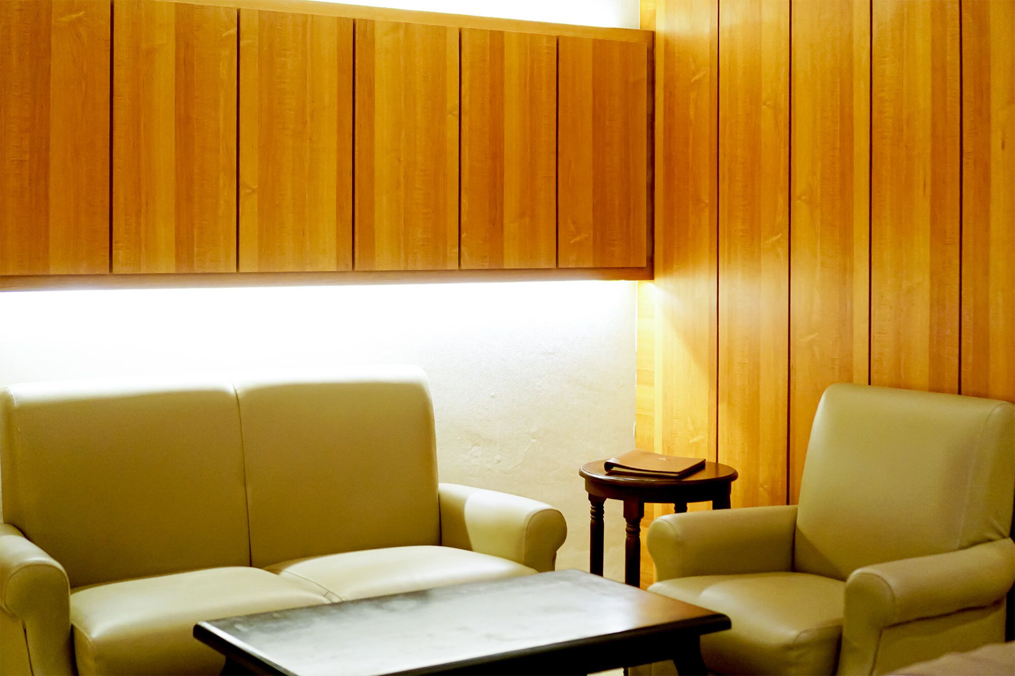 Een kamer met twee leren fauteuils, een tafeltje, houten paneelwanden en een raam dat natuurlijk licht binnenlaat.