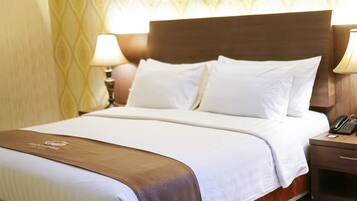 Una cama bien hecha con sábanas blancas y detalles en marrón, una lámpara de noche y un teléfono sobre una mesita de madera.