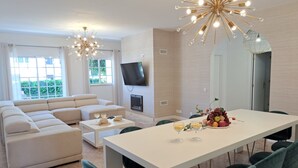 Ein modernes Wohnzimmer mit einer großen Couch, einem Esstisch mit Stühlen, einem Kamin und einem an der Wand befestigten Fernseher.