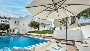 Ein moderner Poolbereich im Freien mit einem weißen Pool, Liegestühlen und einem Tisch mit einem Buch.