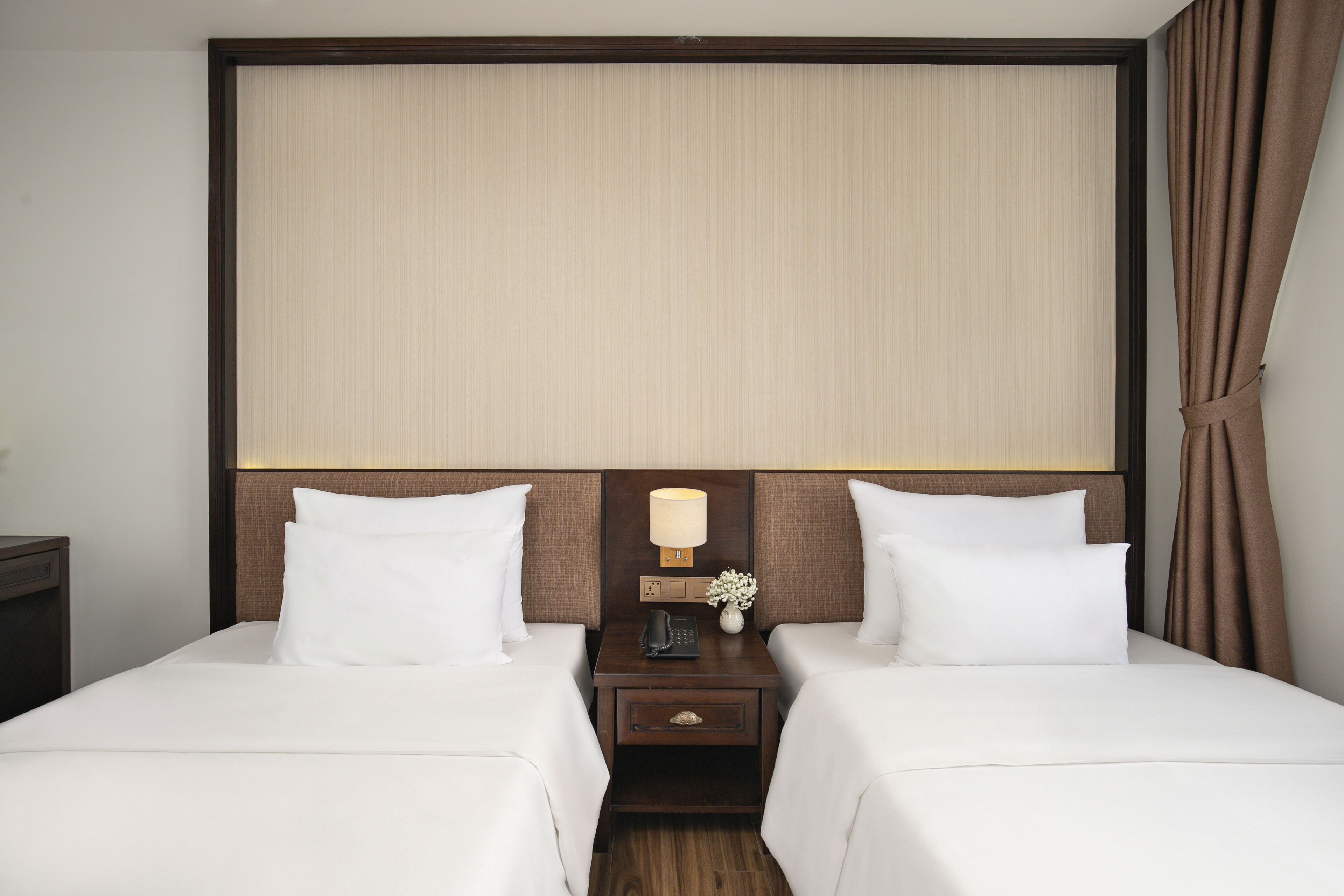 Een hotelkamer met twee bedden, een nachtkastje met een lamp en een wandpaneel.