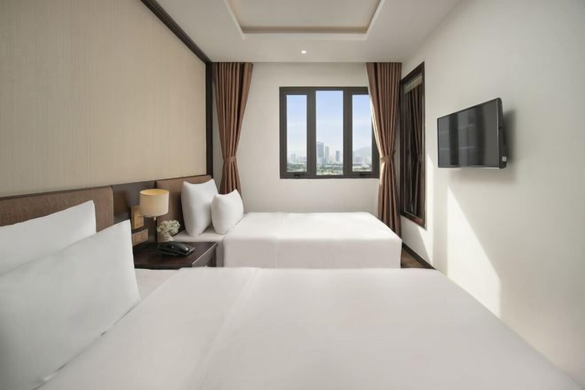 A hotel room with two beds, a TV mounted on the wall, and a window with curtains.