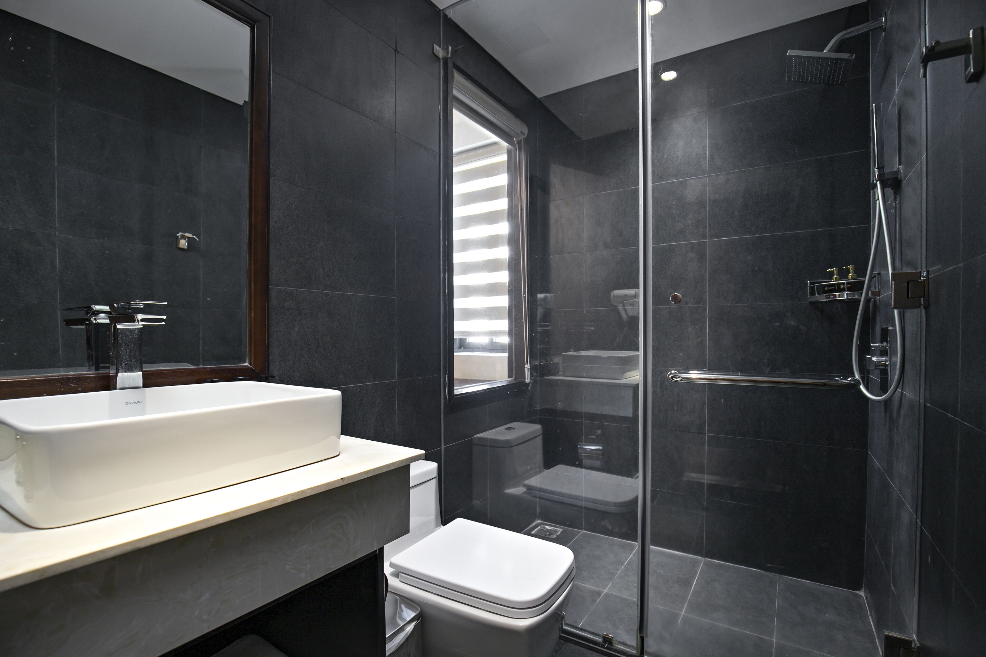 A modern bathroom with a large mirror, a white sink, a toilet, and a glass-enclosed shower area.