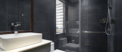 A modern bathroom with a large mirror, a white sink, a toilet, and a glass-enclosed shower area.