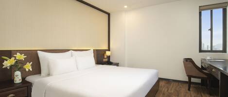 Habitación de hotel con una cama grande, una mesita de noche con un florero, un escritorio con una silla y una ventana con vistas.