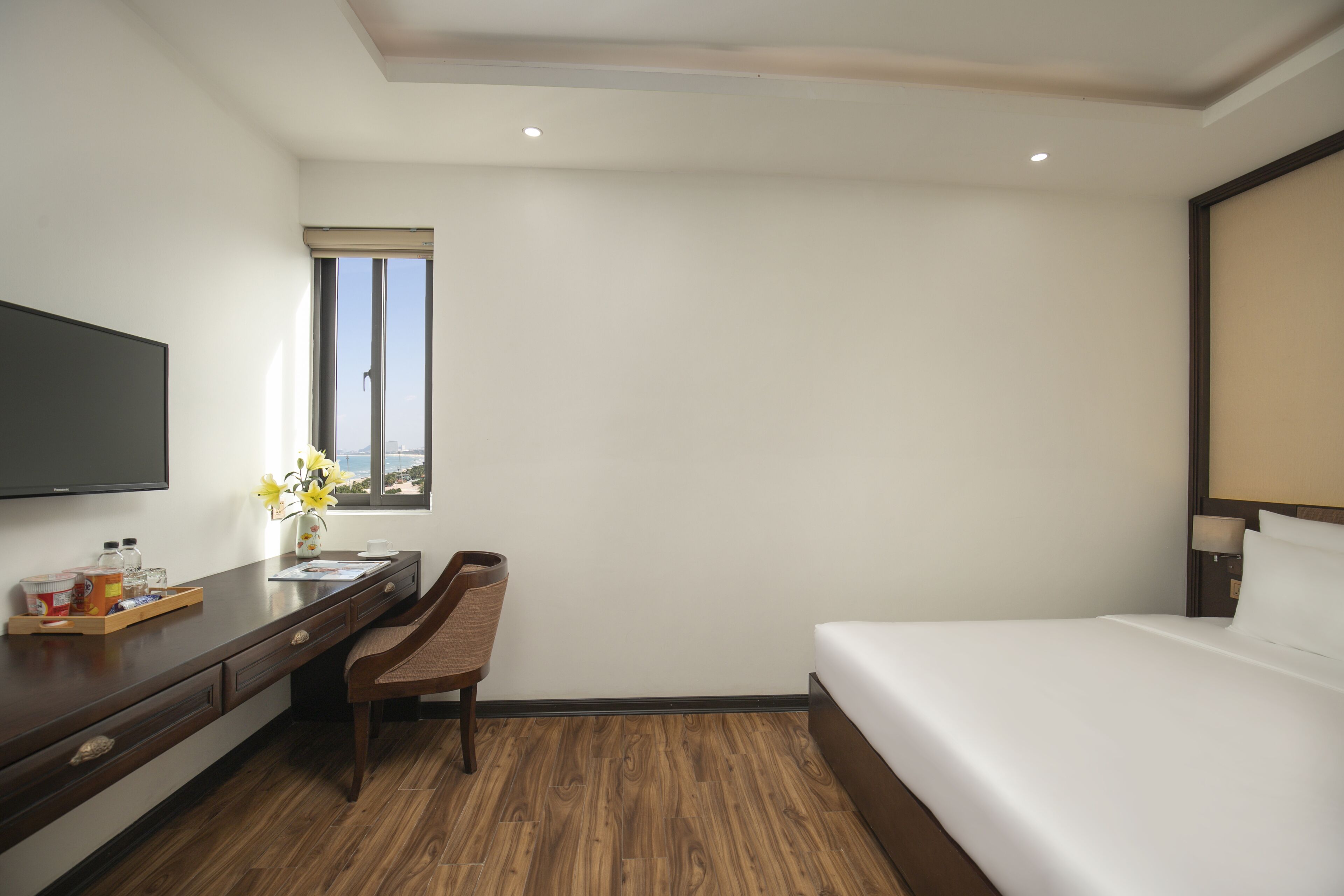 Une chambre d’hôtel comprenant un lit, un bureau avec une chaise, une télévision, une fenêtre avec vue et une petite table avec des articles de toilette.