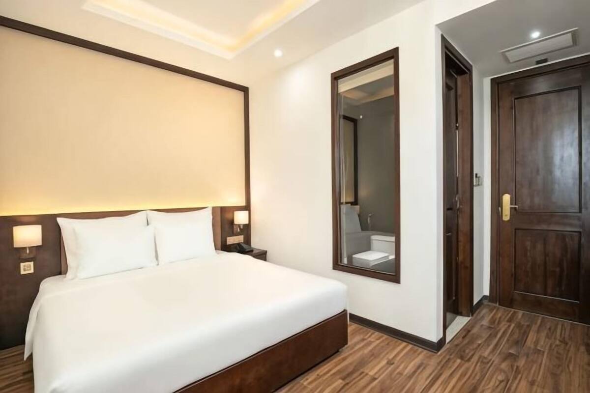 Ein Hotelzimmer mit einem großen Bett, einem Spiegel, Holzboden und einer Tür.