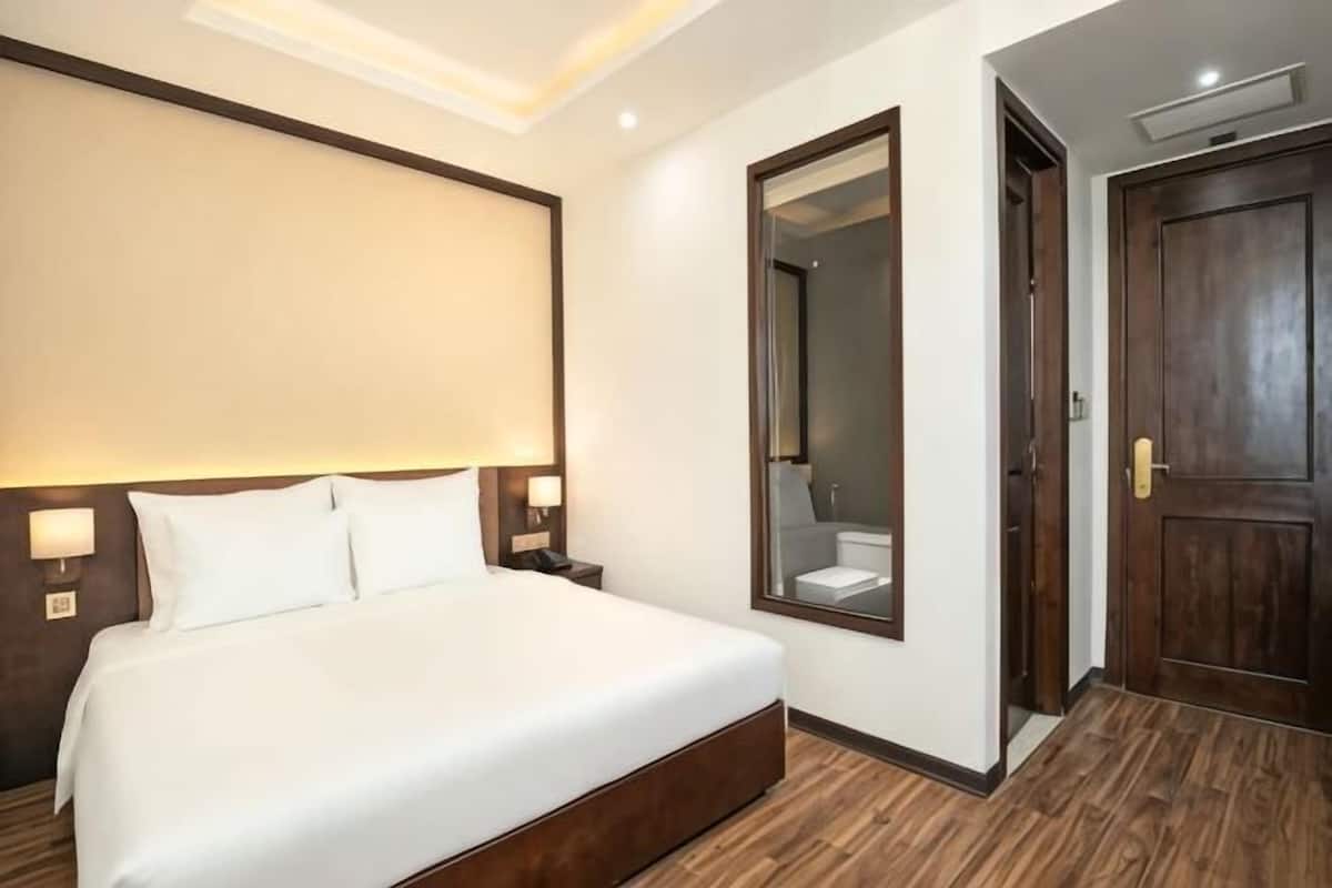 A hotel room with a large bed, a mirror, a wooden floor, and a door.