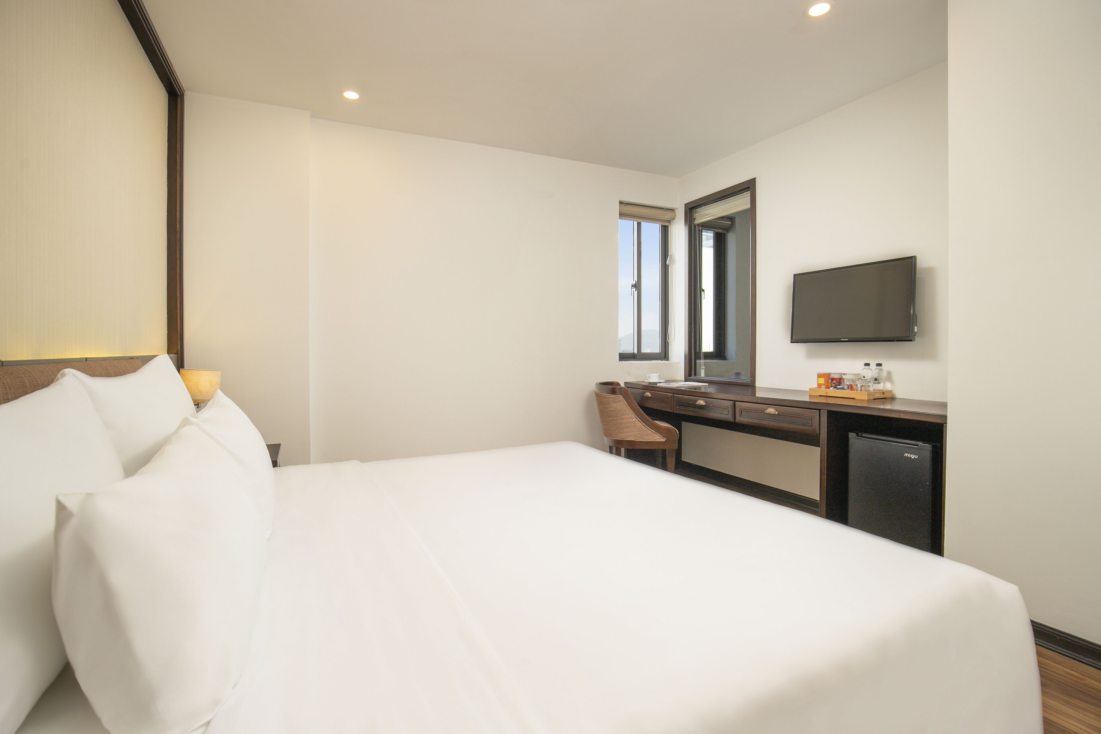 Una habitación de hotel con una cama grande, un escritorio con una silla, un televisor y una ventana.