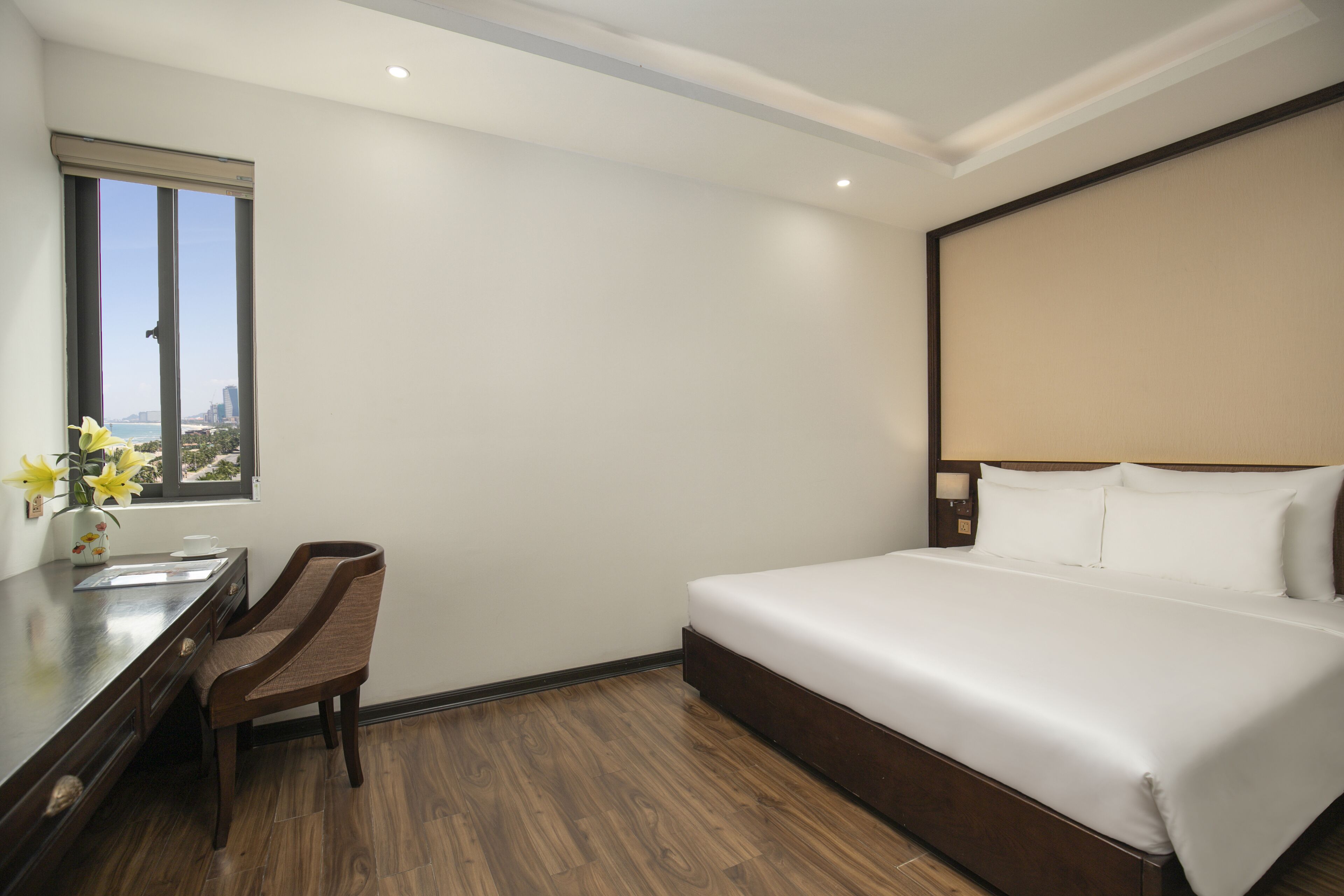 A hotel room with a bed, a desk with a chair, a window with a view, and a nightstand.