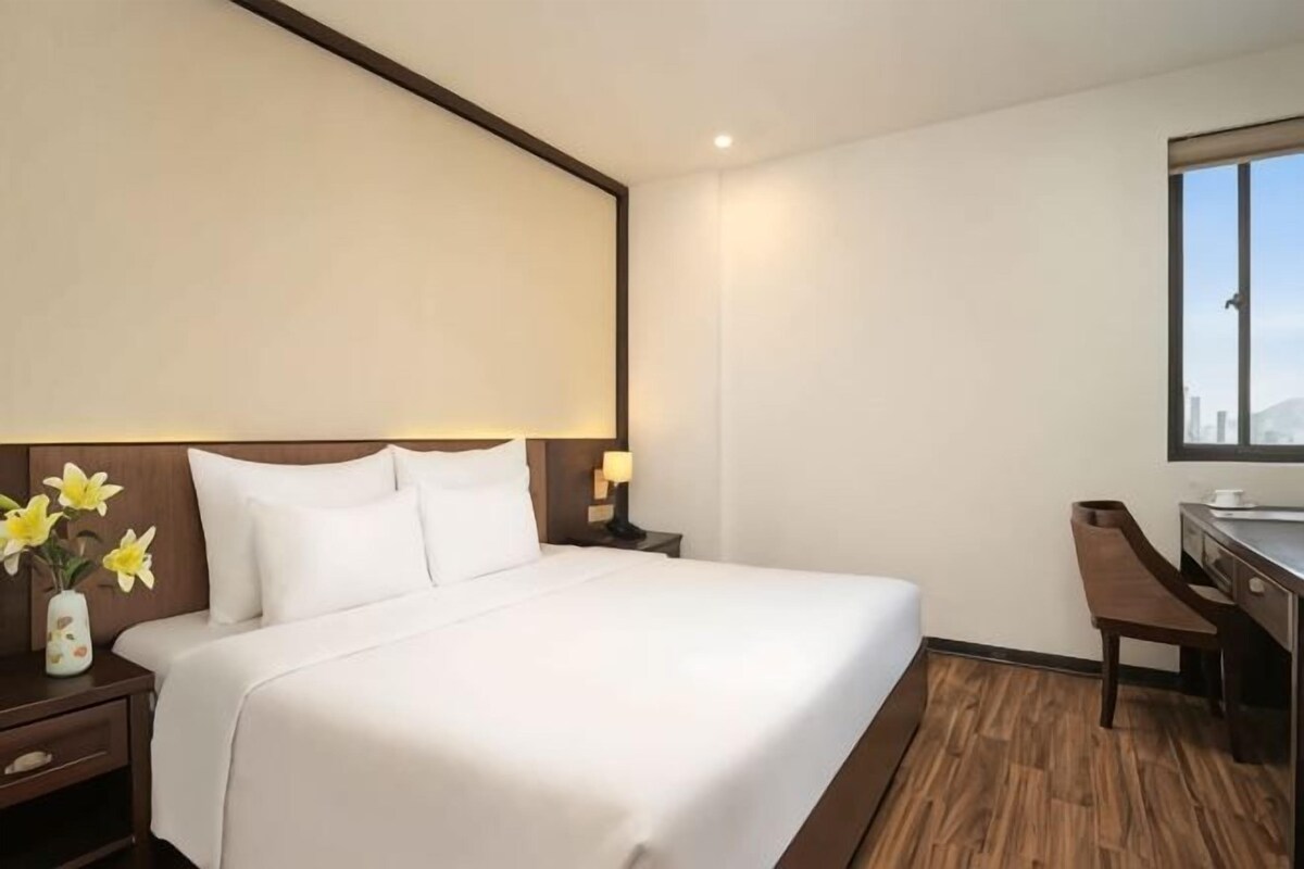 Une chambre d’hôtel avec un grand lit, des tables de chevet, un bureau et une fenêtre.