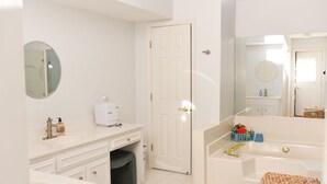 A modern bathroom with a white sink, vanity, and bathtub. There is a door leading to another room, a mirror above the sink, and a small trash bin under the vanity. - MASTER'S TOURNAMENT RENTAL - GATED COMMUNITY - WHOLE HOUSE - 2 OWNER'S SUITES (Martinez)