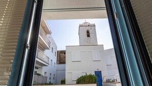 A view through a window of a building with a white facade, a blue door, and a bell tower.