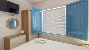 A bedroom with a bed, a dresser, a mirror, and a window with blue shutters.