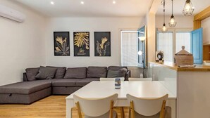 A modern living room with a sectional sofa, a dining table with two chairs, and three framed artworks on the wall.