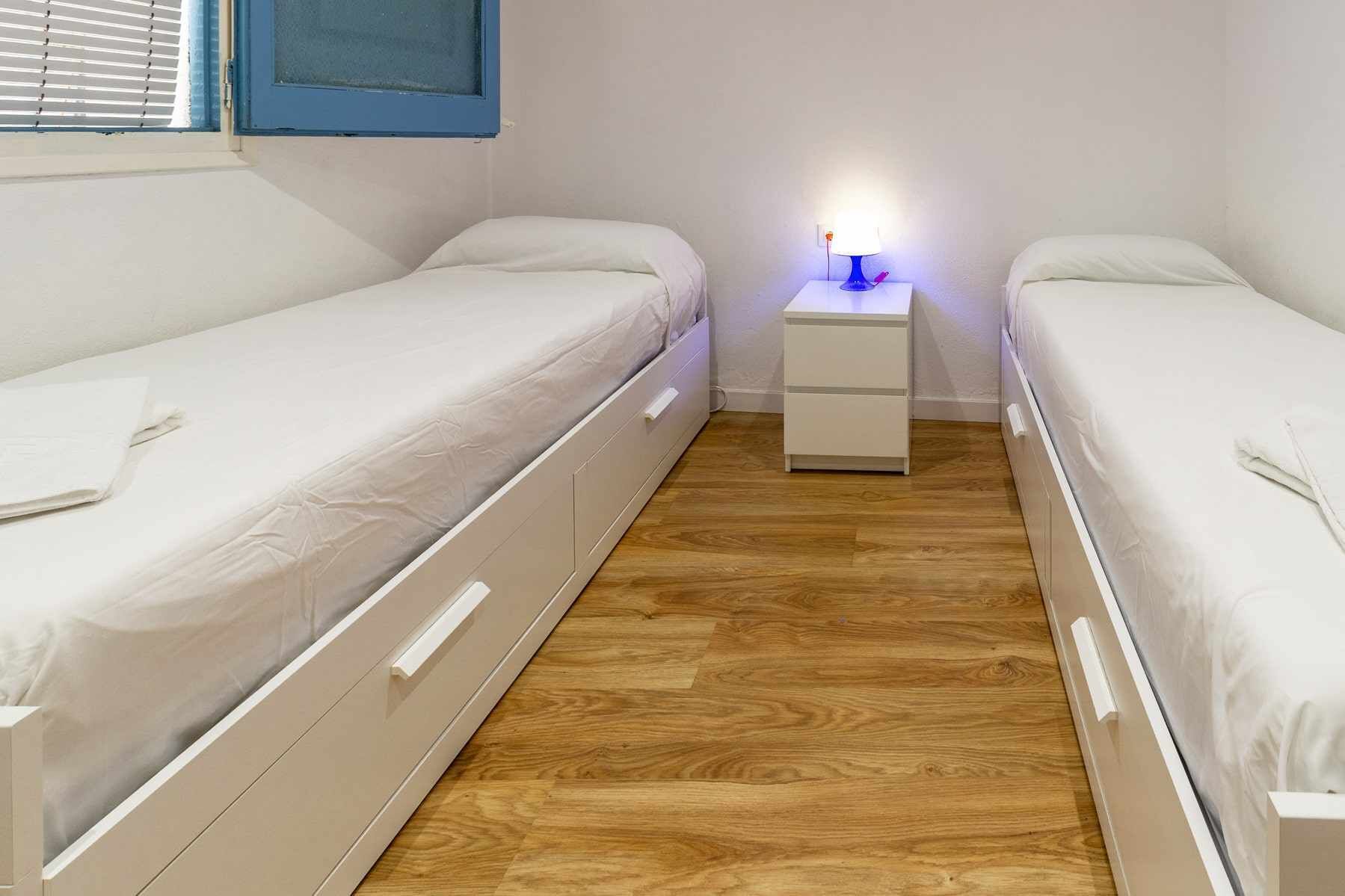 Habitación doble con dos camas individuales, una mesita de noche con lámpara y suelo de madera.