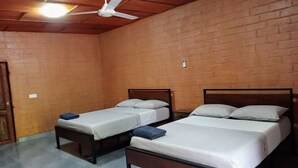 A room with three wooden beds, a ceiling fan, and a brick wall. - Riverside Lodge Bansang (ITC)