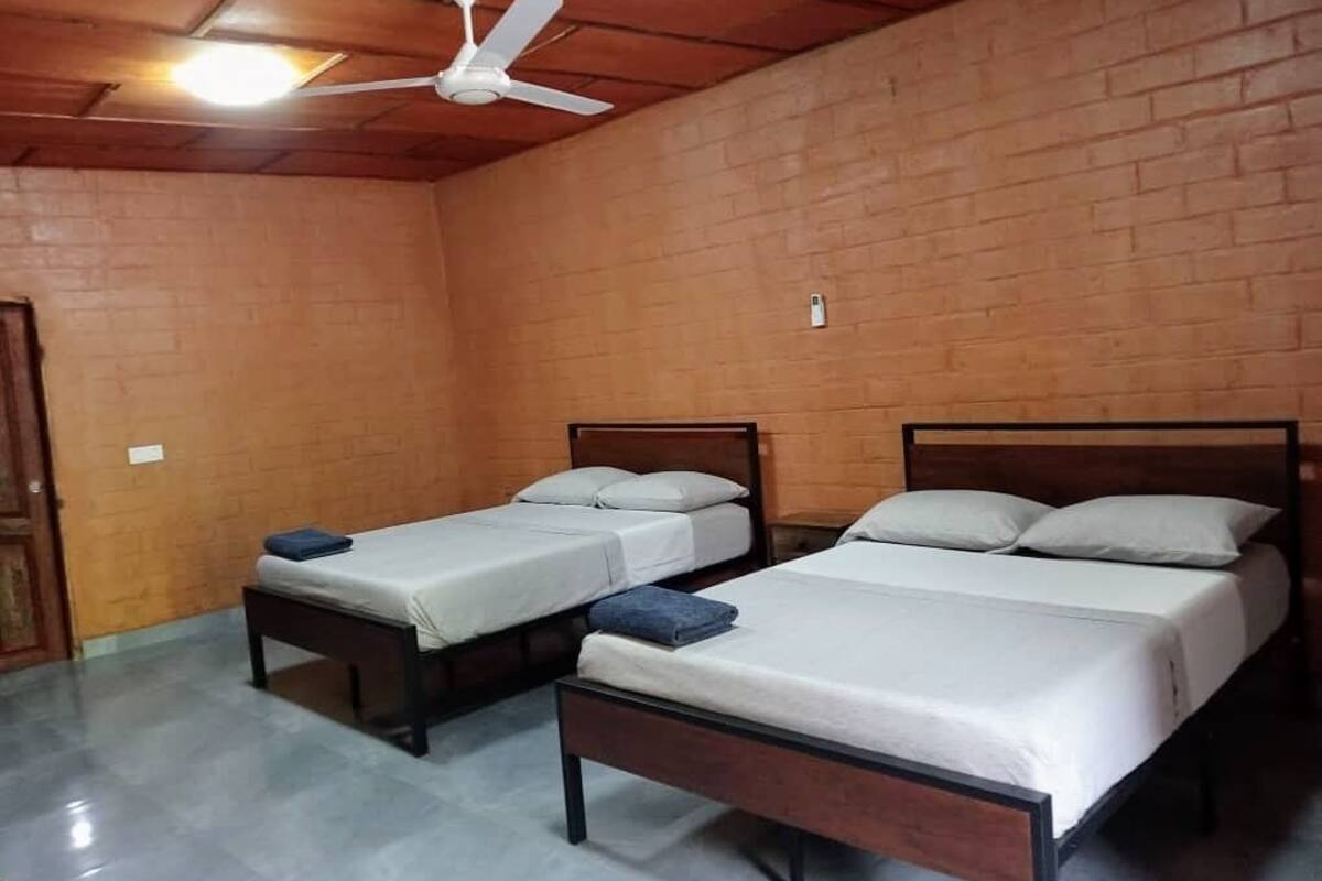 A room with three wooden beds, a ceiling fan, and a brick wall.