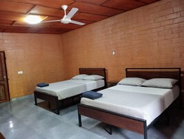 Una habitación con tres camas de madera, un ventilador de techo y una pared de ladrillo.