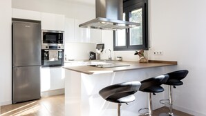 Une cuisine moderne équipée d’un réfrigérateur en acier inoxydable, d’un four encastré, d’un micro-ondes, d’un évier et d’une fenêtre située au-dessus du plan de travail. On y trouve également deux tabourets de bar noirs avec des pieds en métal.