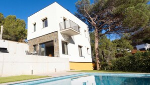 Une maison moderne à deux étages, dotée d’une piscine, d’un balcon et d’une façade en pierre.