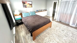 A bedroom with a bed, a ceiling fan, a nightstand, a lamp, a window with curtains, and a wall-mounted picture. - Highland Hideaway-Newly Remodeled!  (Sheridan)