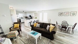 A modern living room with a sofa, coffee table, and chairs, a kitchen in the background, and a dining area with a table and chairs. - Highland Hideaway-Newly Remodeled!  (Sheridan)