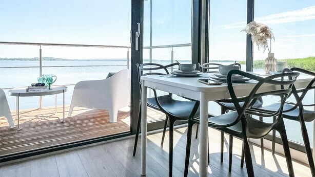 Un espace repas avec une table et des chaises, donnant sur un plan d’eau.